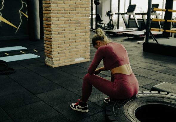 A woman in sportswear rests on a tire during gym training, showcasing fitness dedication.