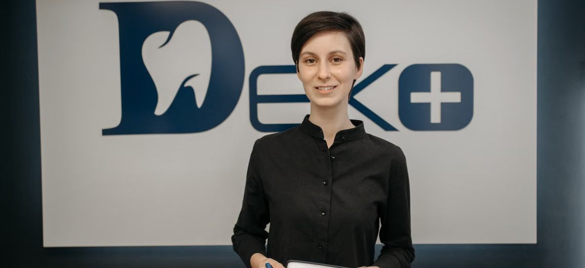 Smiling dentist holding a notebook in front of a clinic sign, promoting a welcoming and professional dental environment.