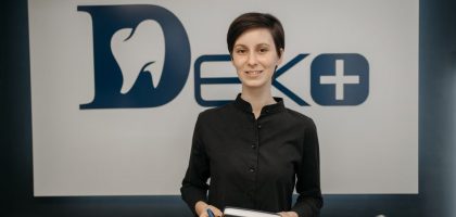 Smiling dentist holding a notebook in front of a clinic sign, promoting a welcoming and professional dental environment.