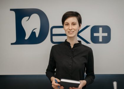 Smiling dentist holding a notebook in front of a clinic sign, promoting a welcoming and professional dental environment.
